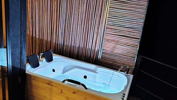 A wooden spa tub with a built-in seat and controls, set against a backdrop of bamboo slats and a corrugated metal roof. - COCOZNA Glamping (Samaná)