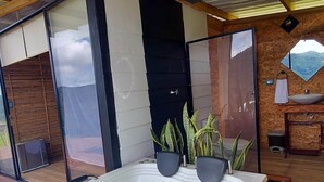 A modern bathroom with a large bathtub, wooden flooring, and a view of the outdoors. - COCOZNA Glamping (Samaná)