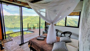 A bedroom with a large bed, a canopy, and a view of a lake and mountains. - COCOZNA Glamping (Samaná)