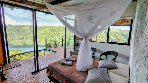 A bedroom with a large bed, a canopy, and a view of a lake and mountains. - COCOZNA Glamping (Samaná)