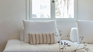 A modern living room with a white sofa, two pillows, a small white vase with branches, and a wooden coffee table.