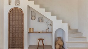 A staircase with a white wall, a wooden door, and a shelf with books and vases.