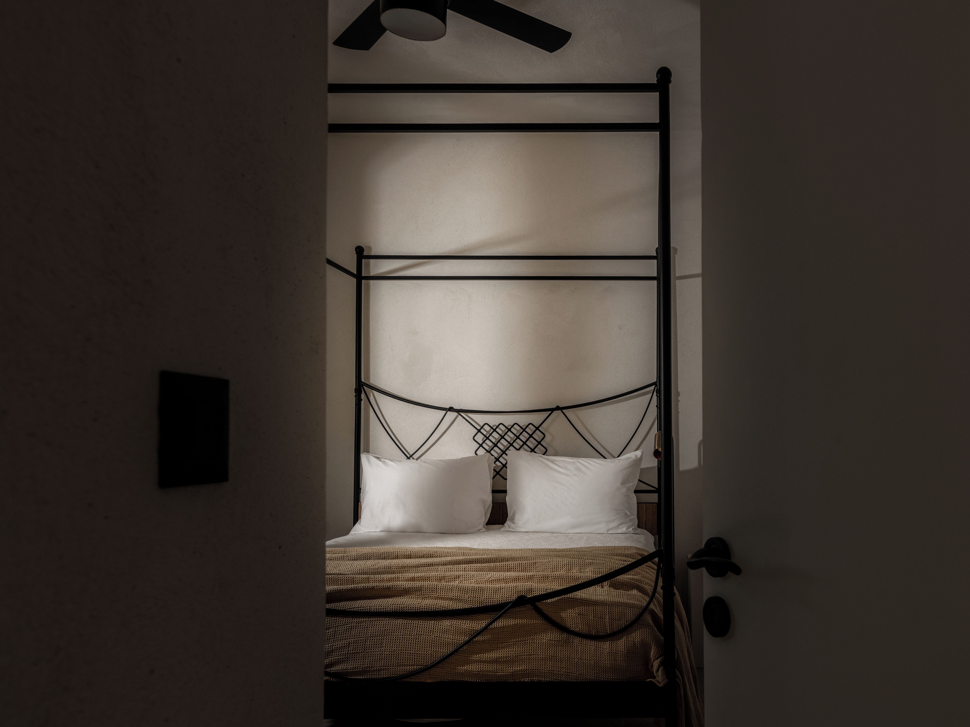 Un letto a baldacchino in metallo con lenzuola bianche e una coperta tessuta, in una stanza poco illuminata.