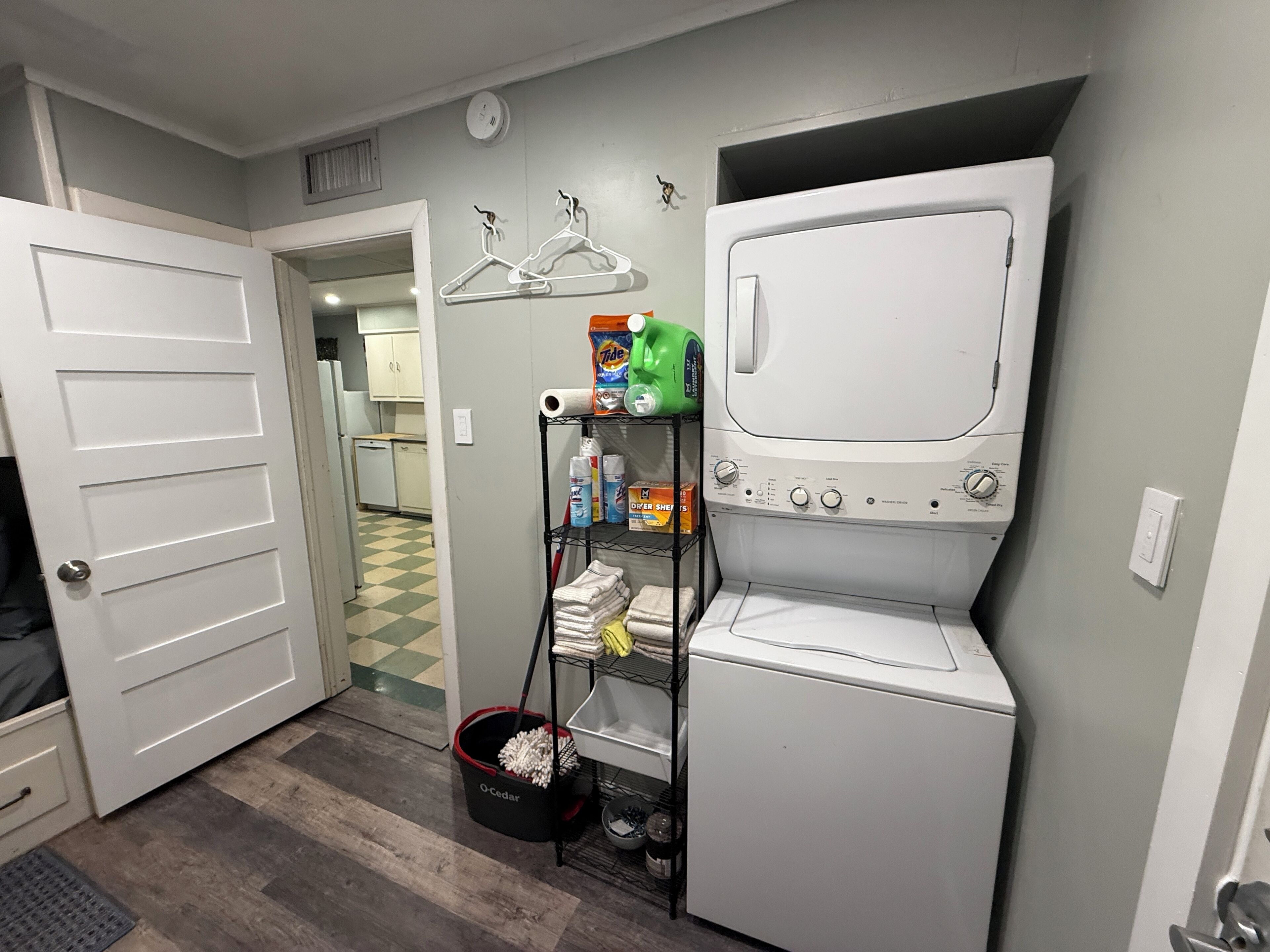 A laundry room with a washer and dryer, a shelf with cleaning supplies, and a checkered floor.