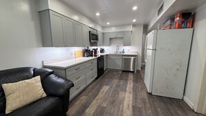 A modern kitchen with grey cabinets, a black leather couch, and a white refrigerator.