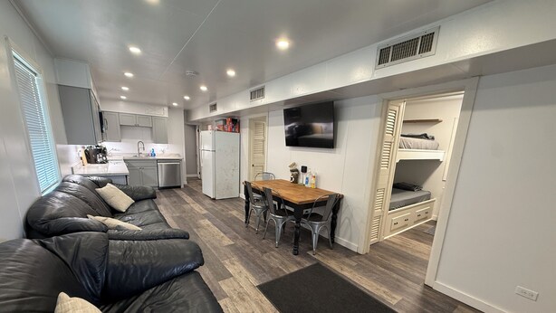 A compact living space with a sofa, dining table, kitchen area, and a TV mounted on the wall.