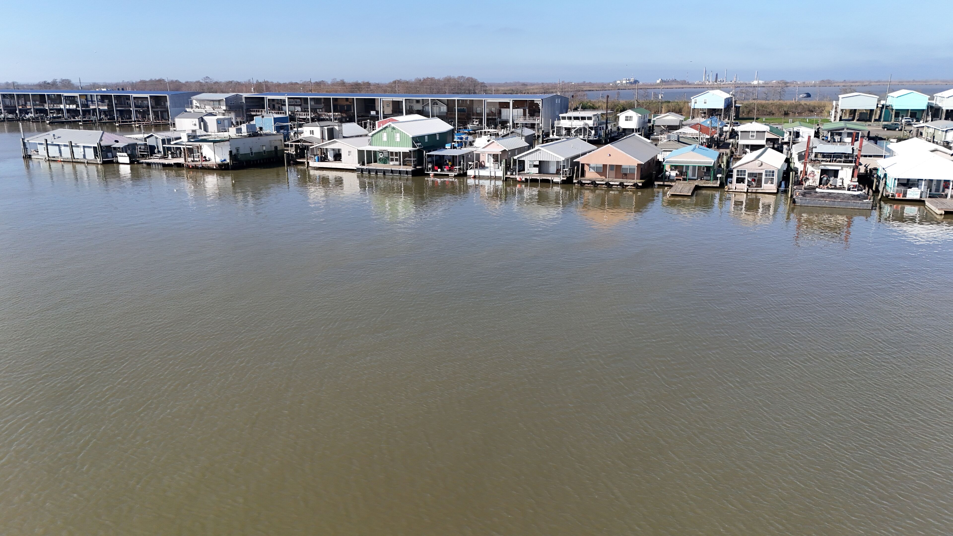 A waterfront property with multiple floating homes connected by walkways, featuring a marina and a distant industrial area.