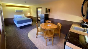 A compact hotel room with a bed, a small dining table with chairs, a refrigerator, a microwave, and a sink. - Thousand Hills (Kirksville)