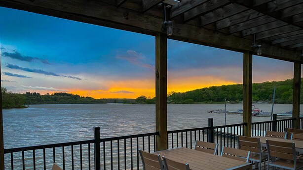 A wooden deck with tables and chairs overlooking a lake at sunset. - Thousand Hills (Kirksville)