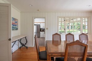 A dining area with a wooden table and chairs, a view of the kitchen through an open door, and a painting on the wall.