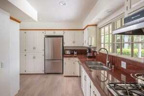 Una cocina moderna con gabinetes blancos, electrodomésticos de acero inoxidable, una estufa a gas y un amplio ventanal que proporciona luz natural.