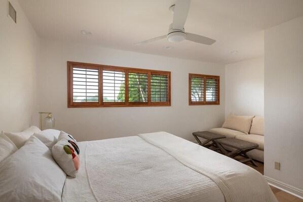Un dormitorio con cama, dos ventanas, ventilador de techo y sofá.