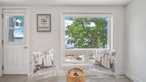 A room with two clear chairs, a wicker basket, a door with a window, and a wall with a 'Sardines' sign.