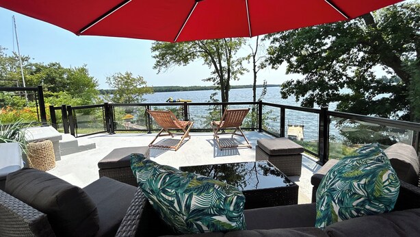 A balcony with wicker furniture, a red umbrella, and a view of a lake.