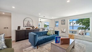 A modern living room with a blue sofa, a coffee table, and a view of the water through large windows.
