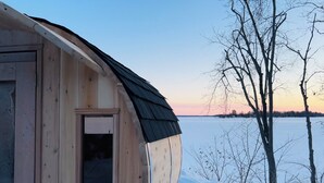 A wooden cabin with a large window, a curved roof, and a view of a frozen lake.
