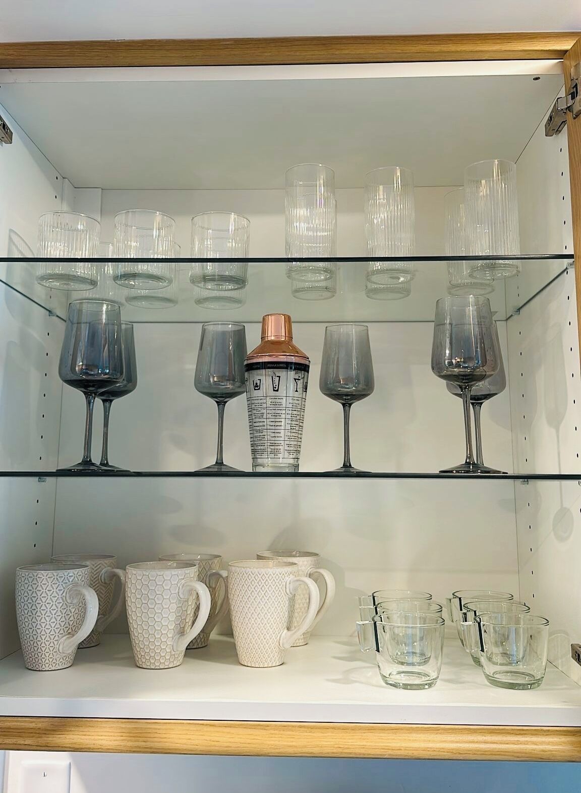 A shelf with various glassware, including wine glasses and tumblers, and patterned mugs.