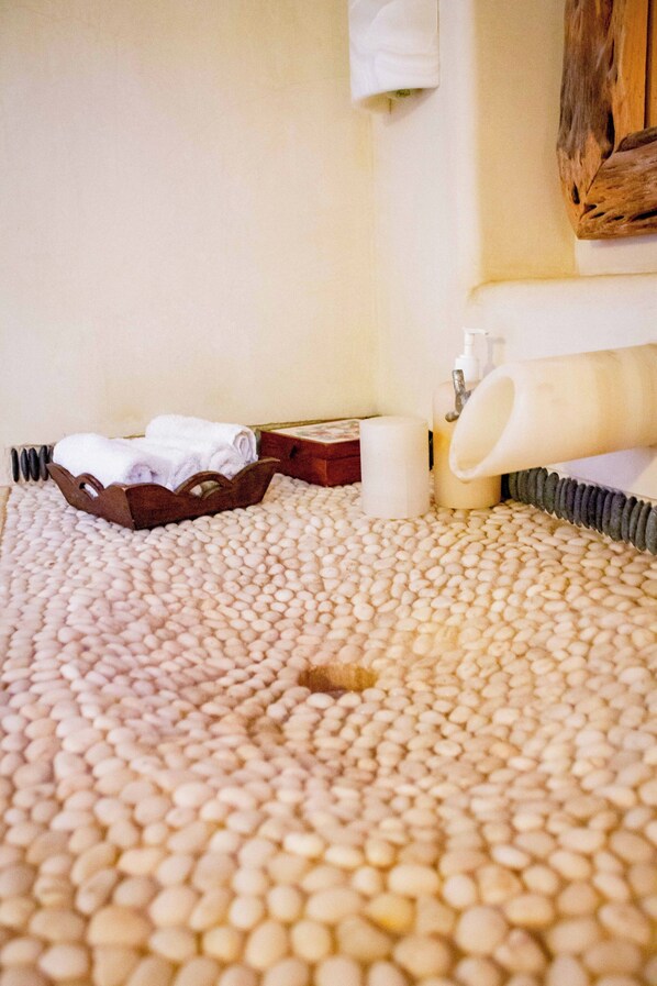Une salle de bain avec un sol beige à texture, un tapis de bain en bois, un porte-serviettes et une serviette blanche.