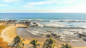 Una spiaggia con costa rocciosa, palme e acqua cristallina.