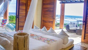 Una camera da letto con un letto grande, persiane in legno e vista sull'oceano.