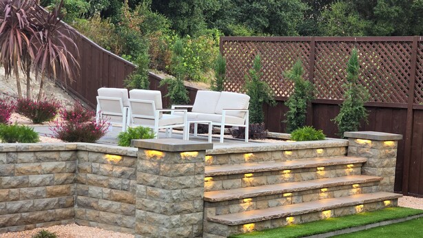 Un jardin avec un mur en pierre, un espace salon extérieur et une clôture en bois.