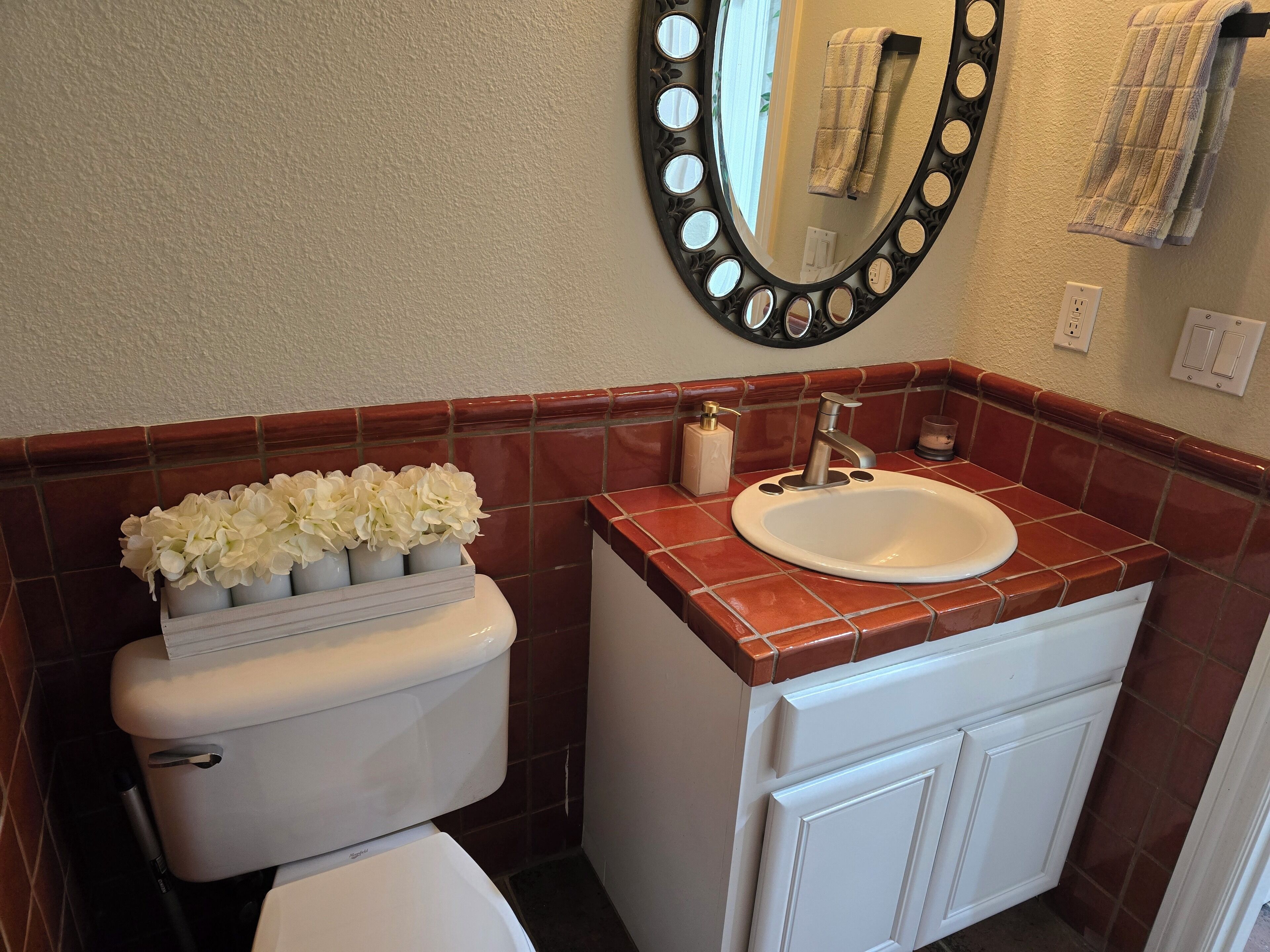 Un baño con un inodoro blanco, un lavamanos con un espejo encima y una pequeña planta sobre el tanque del inodoro.