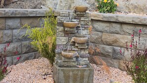 Une fontaine en pierre à plusieurs niveaux, avec un bassin central, entourée de galets et de plantes.