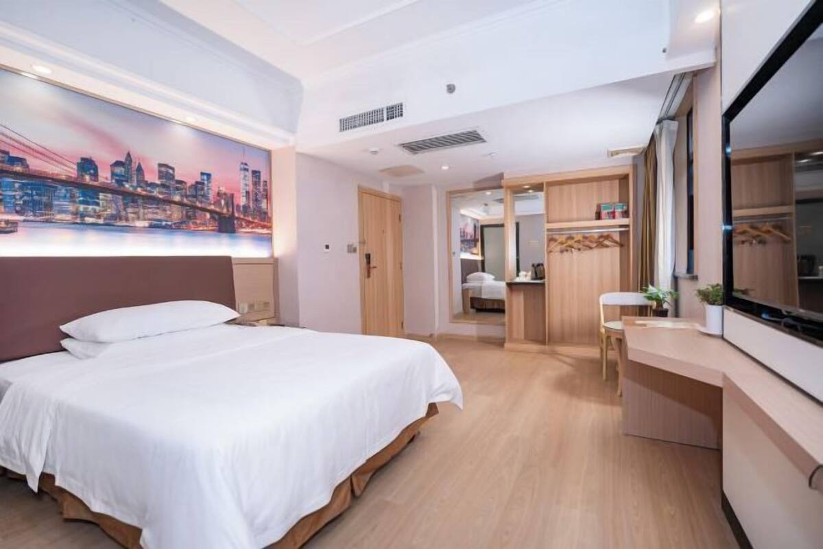 A hotel room with a bed, a desk, and a cityscape painting on the wall.