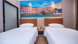 Et hotelværelse med to senge, et stort maleri af et bybillede og et natbord med telefon og lampe.