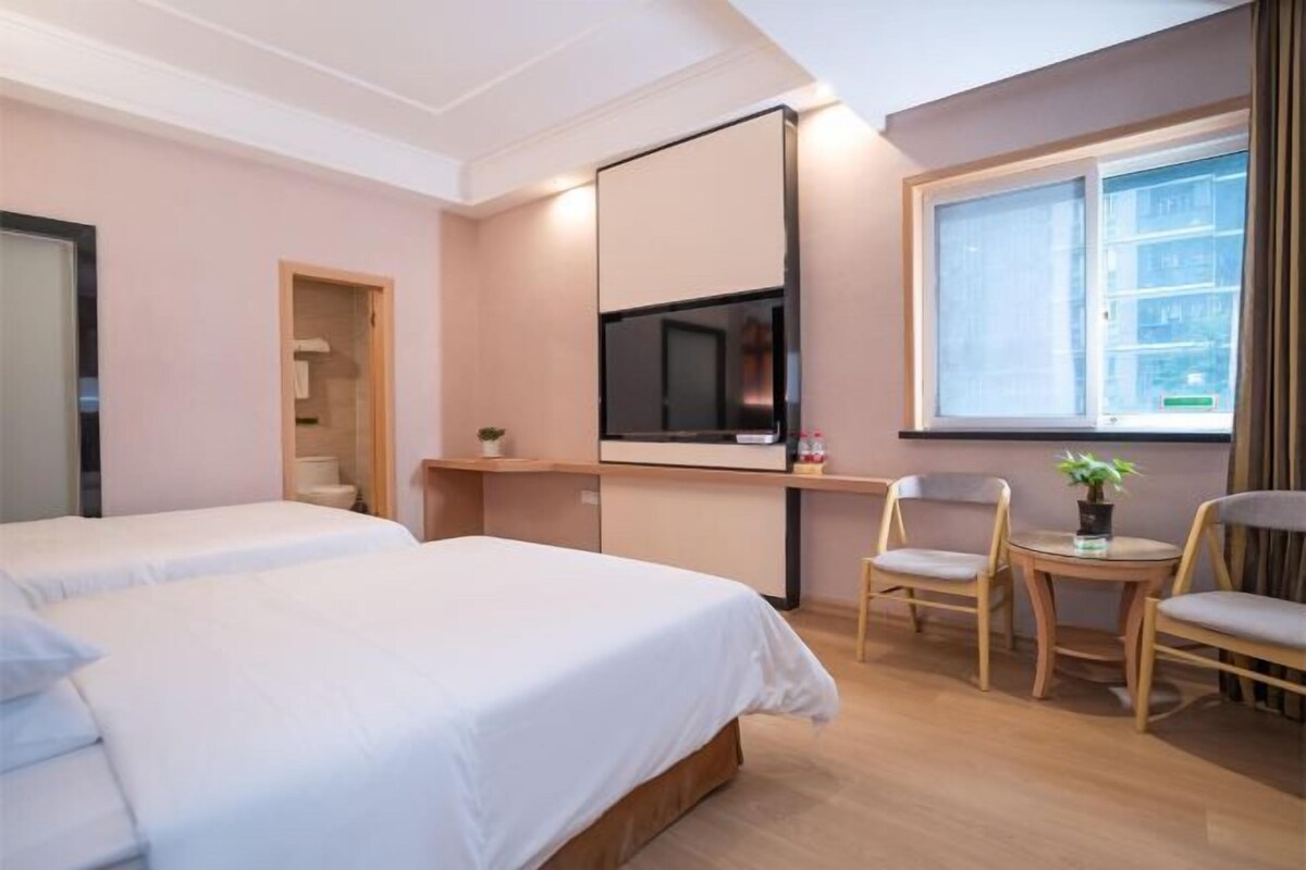 A hotel room with two beds, a TV, a window, and a small table with chairs.