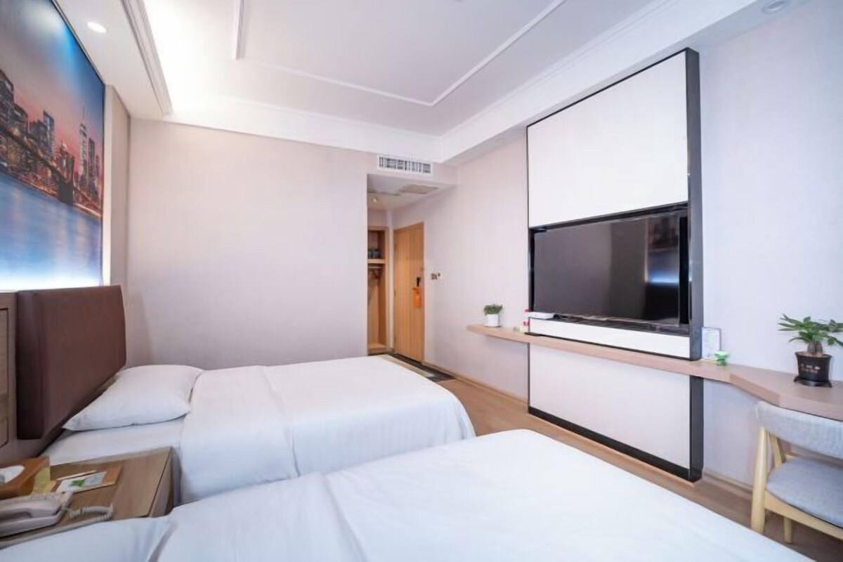 A hotel room with two beds, a TV mounted on the wall, a small desk, and a painting on the wall.