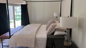 Un letto a baldacchino con tenda, un comodino con lampada e vista sull'esterno attraverso un'ampia finestra.