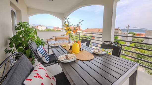 A balcony with a dining table, chairs, and a potted plant.