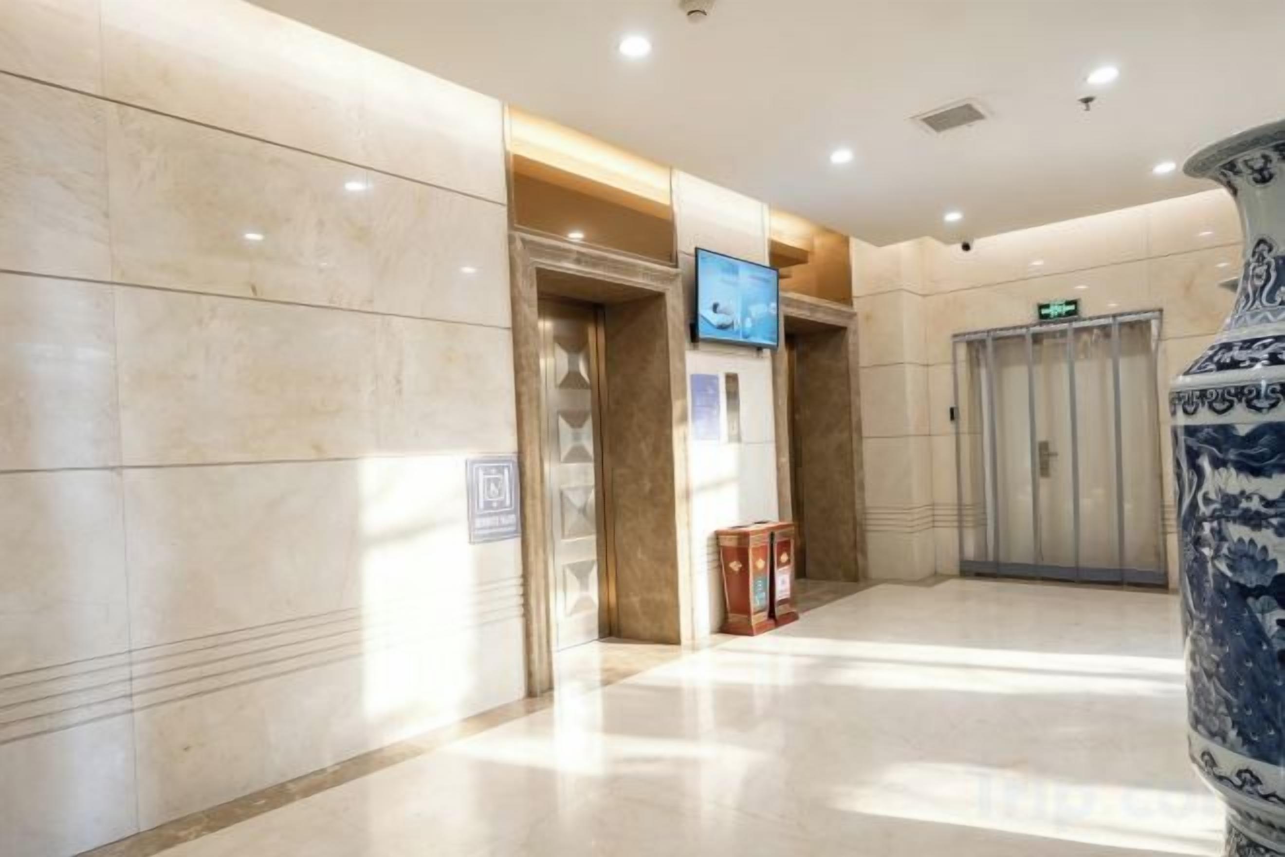 A hotel lobby with a marble floor, a reception desk, a television screen, and a decorative vase.