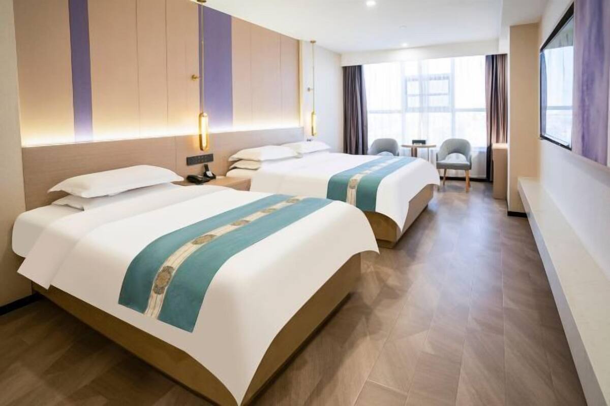 A hotel room with two beds, a desk, a chair, and a large window.
