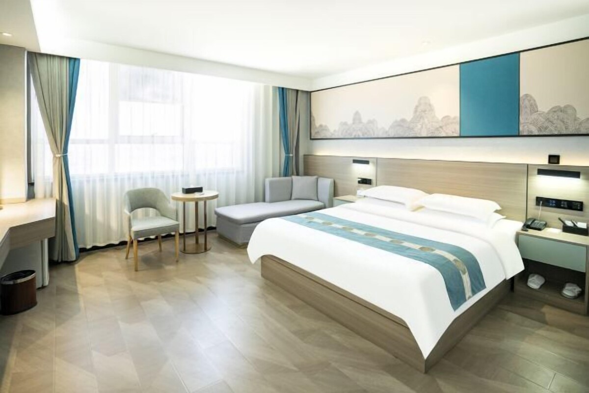 A modern hotel room with a large bed, a desk, a chair, and a small table.