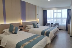 Habitación de hotel con dos camas, un escritorio, una silla y un ventanal grande con cortinas.