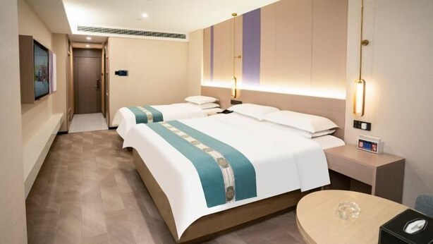 Quarto de hotel com duas camas, uma mesa pequena, uma mesinha de cabeceira e uma luminária fixa na parede.