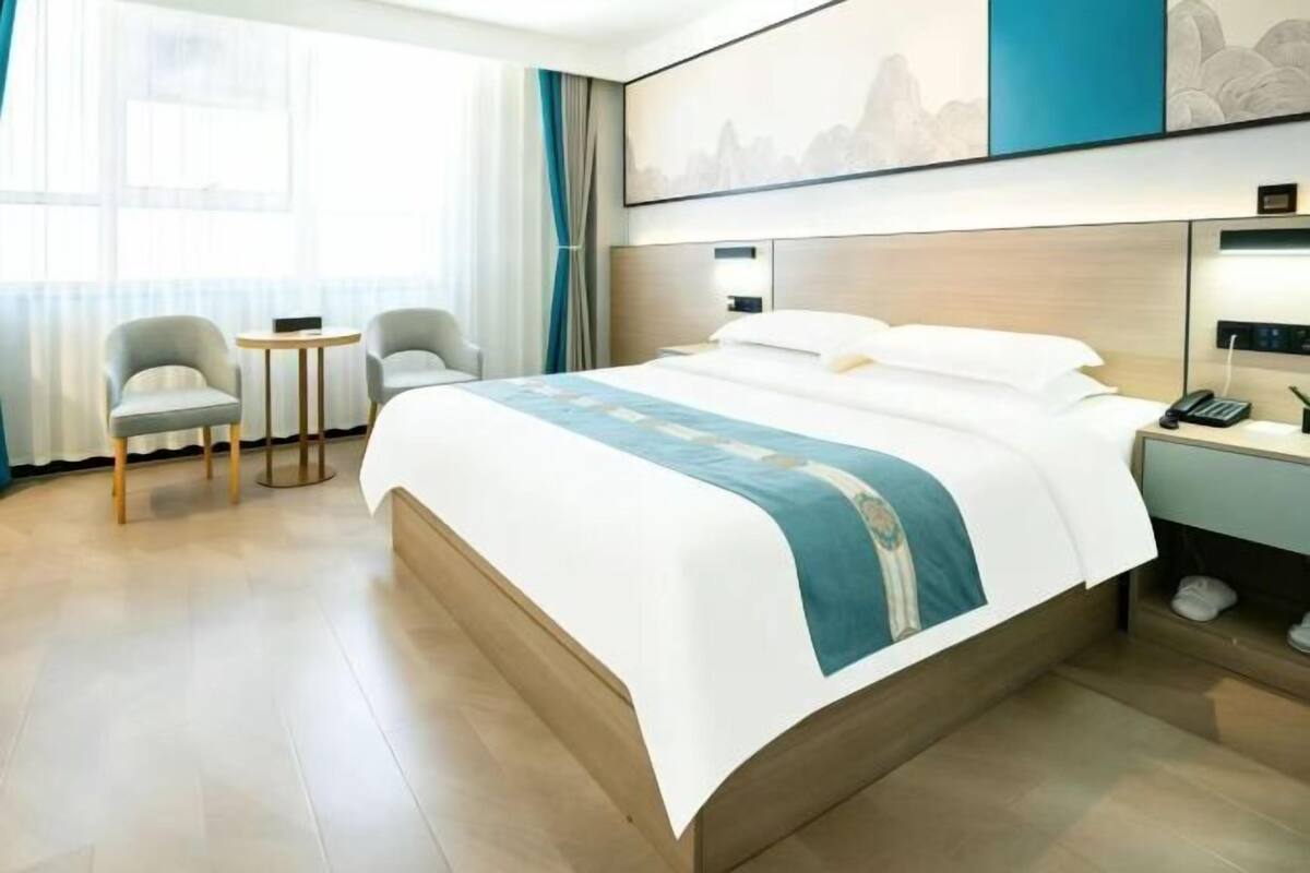 A hotel room with a large bed, two armchairs, a small table, a bedside table with a lamp, and a painting on the wall.