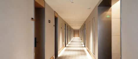 A hotel corridor with doors on both sides, a patterned floor, and a ceiling with recessed lighting.