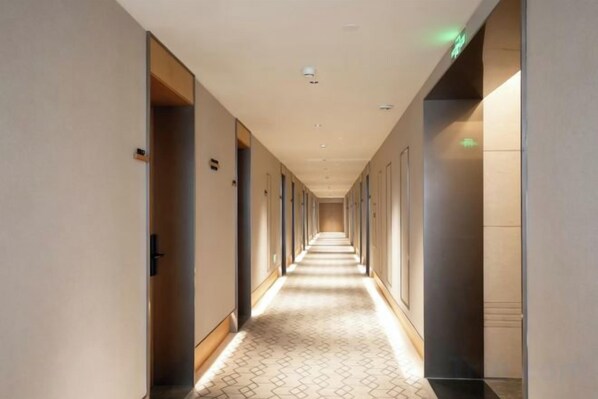 A hotel corridor with doors on both sides, a patterned floor, and a ceiling with recessed lighting.