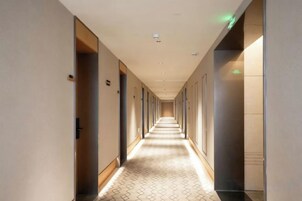 Un pasillo de hotel con puertas a ambos lados, piso estampado e iluminación empotrada en el techo.