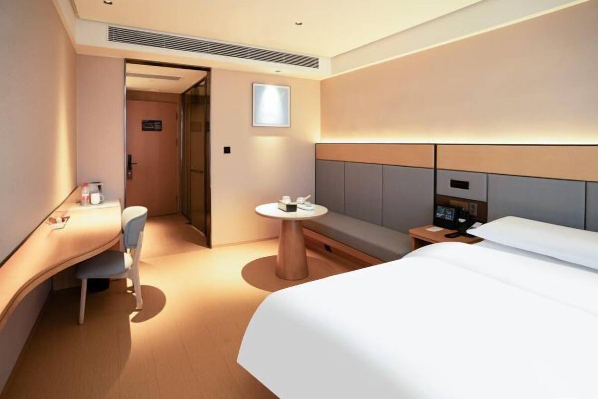 A modern hotel room with a large bed, a desk with a chair, a small round table, and a bedside table with a phone.