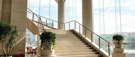 A grand staircase in a hotel lobby with large windows and potted plants.