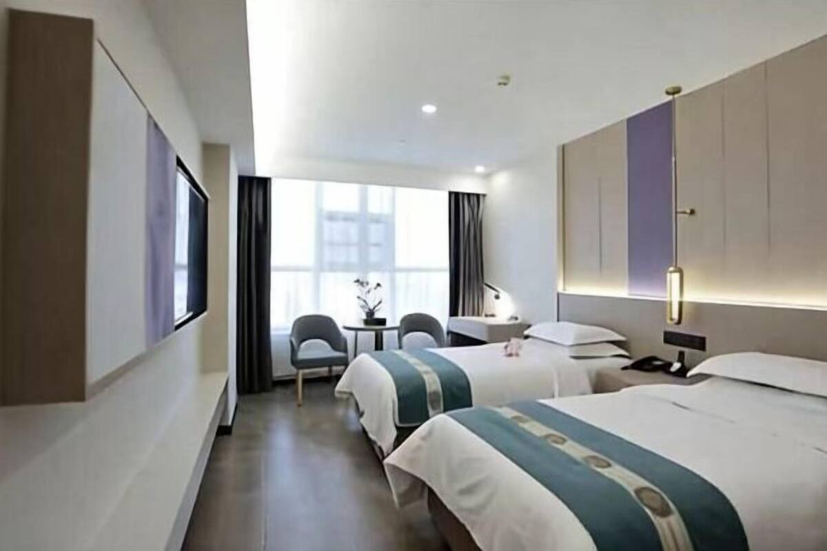 A hotel room with two beds, a desk, a chair, and a window with curtains.