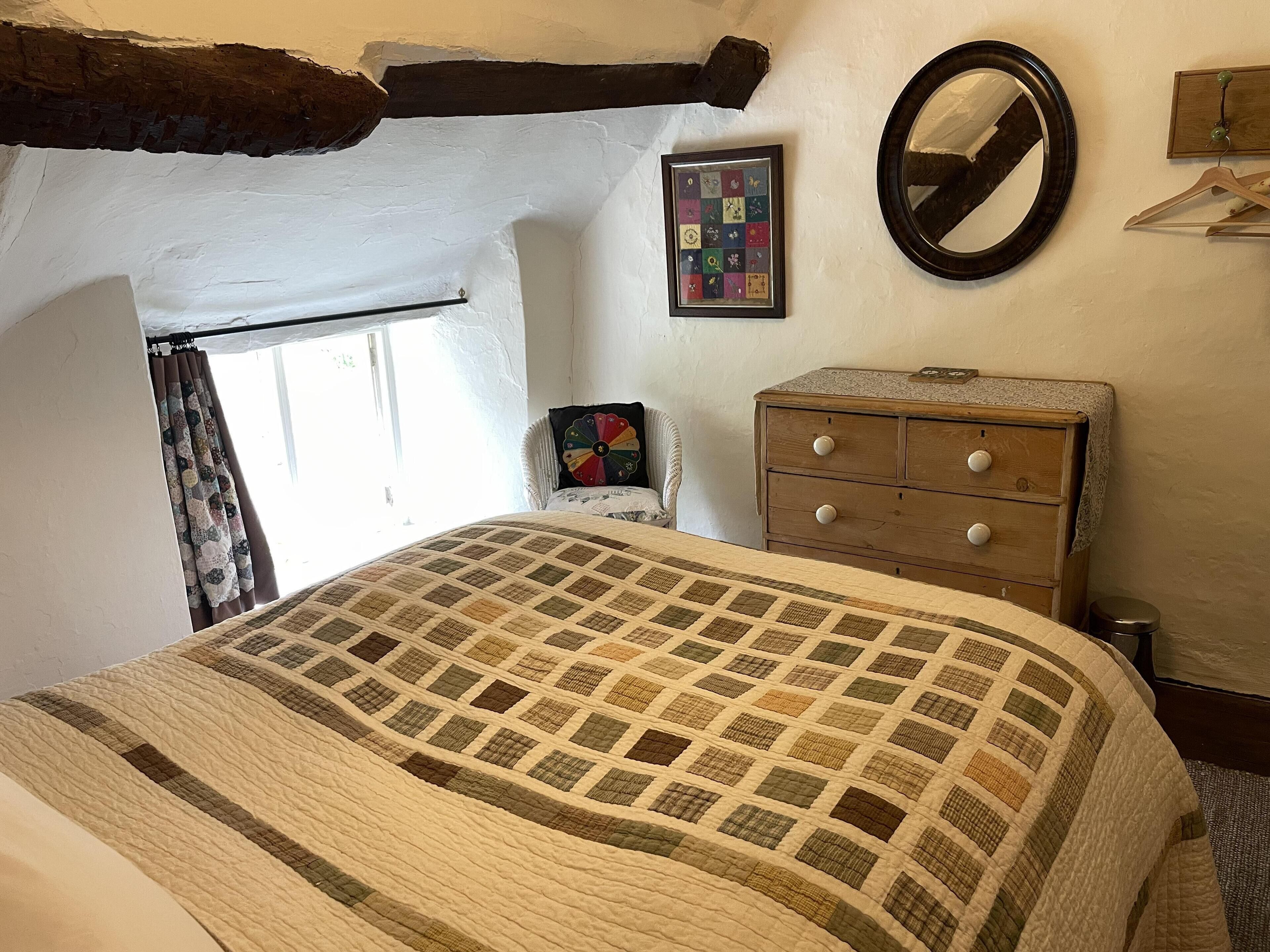 A bedroom with a quilted bedspread, a wooden dresser, a mirror, and a framed picture on the wall.