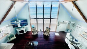 Una habitación con vista al océano, suelo de madera, ventilador de techo y una zona de comedor con mesa para cuatro.