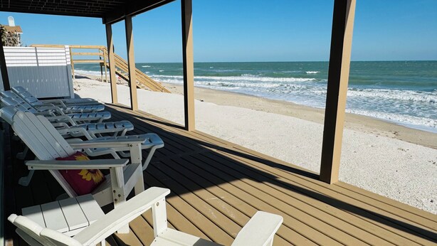 Un salón junto a la playa con sillones blancos y una terraza de madera.
