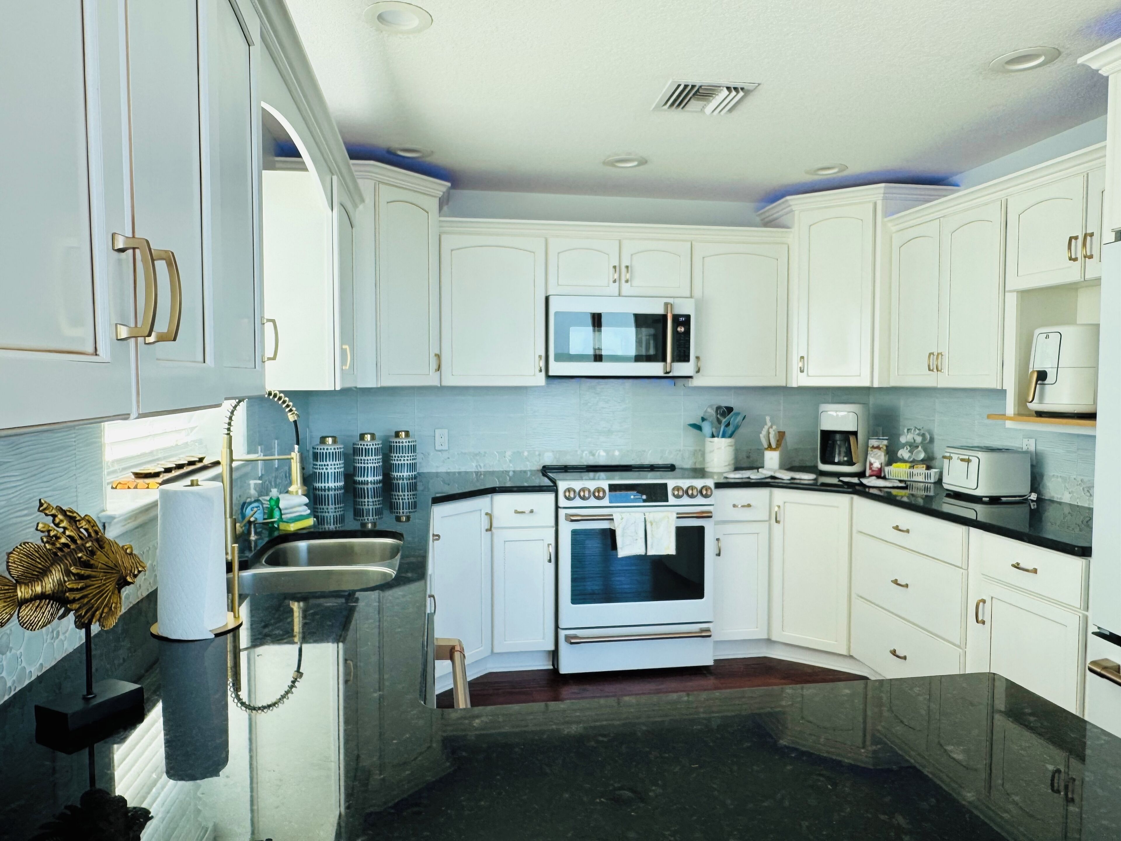 Una cocina moderna con gabinetes blancos, un lavamanos de acero inoxidable, horno empotrado, microondas y cafetera.