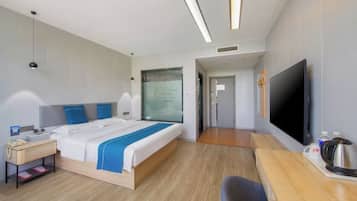 Ein modernes Hotelzimmer mit einem großen Bett, Nachttisch, Flachbildfernseher und Schreibtisch mit Stuhl.